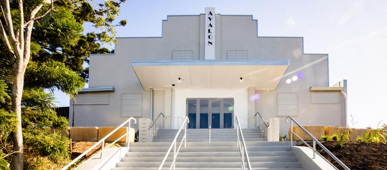 A white theatre with a sign on the roof that reads "avalon" 